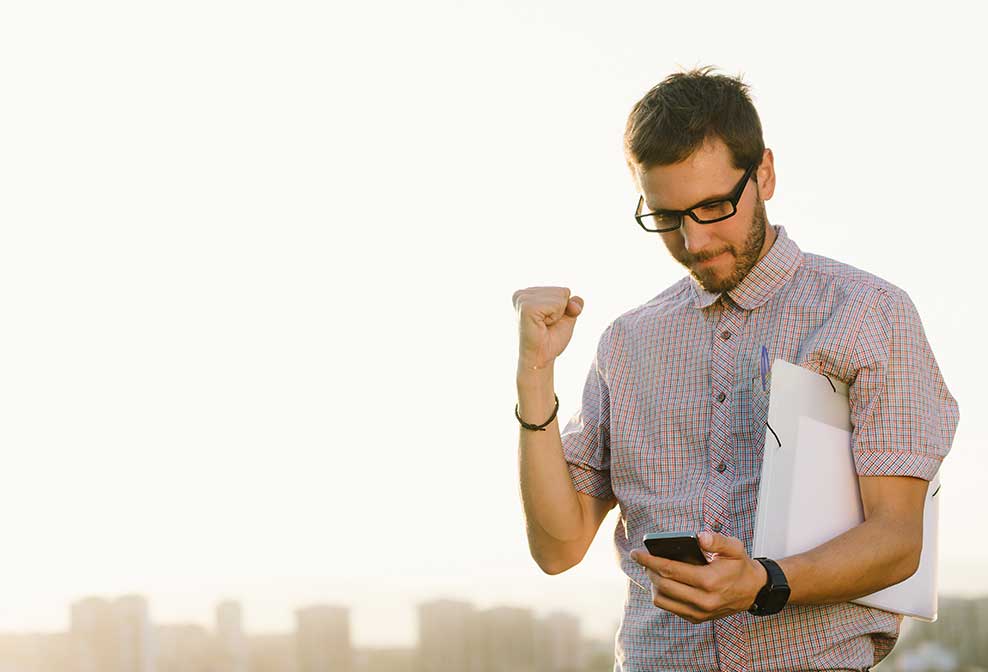 Mann freut sich über positive Nachricht auf Smartphone