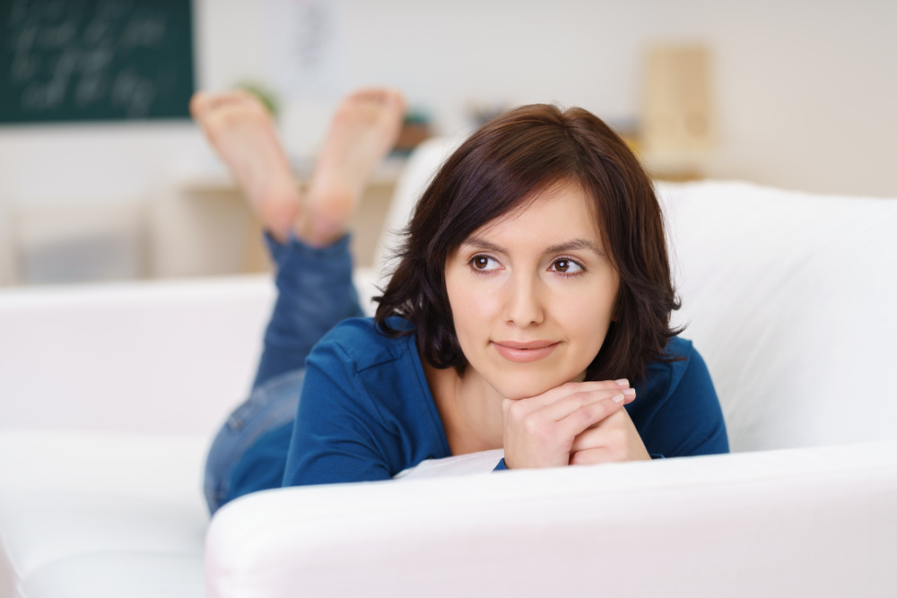 Frau liegt lächelnd auf einem Sofa.